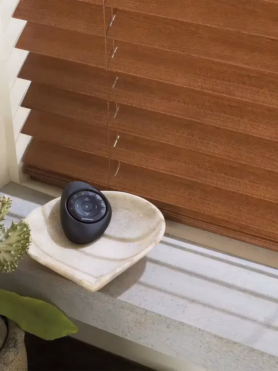 PowerView Pebble Remote on stone dish beside mahogany wood blinds